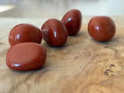 Pierres roulées en jaspe rouge naturel de qualité A, aux nuances rouge brique, disposées sur un fond en bois clair.