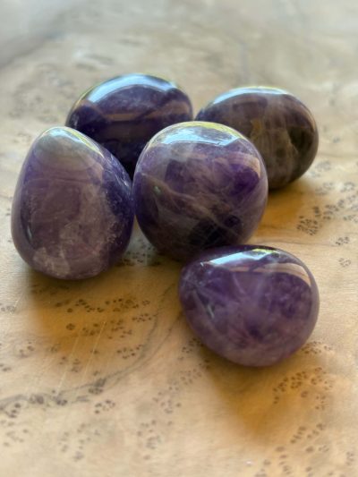 Pierres roulées d'améthyste naturelle violette de qualité A disposées sur un fond en bois clair.