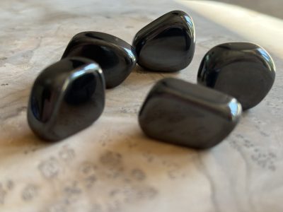 Pierres roulées en hématite naturelle de qualité A+, aux reflets gris métallisés, disposées sur un fond en bois clair.
