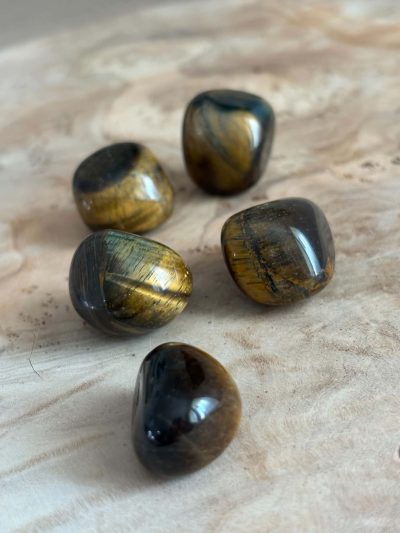 Pierres roulées en œil de tigre naturel de qualité A, aux nuances dorées et brunes chatoyantes, disposées sur un fond en bois clair.