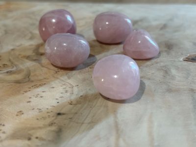 Pierres roulées en quartz rose naturel de qualité A, aux douces nuances de rose pâle, disposées sur un fond en bois clair.